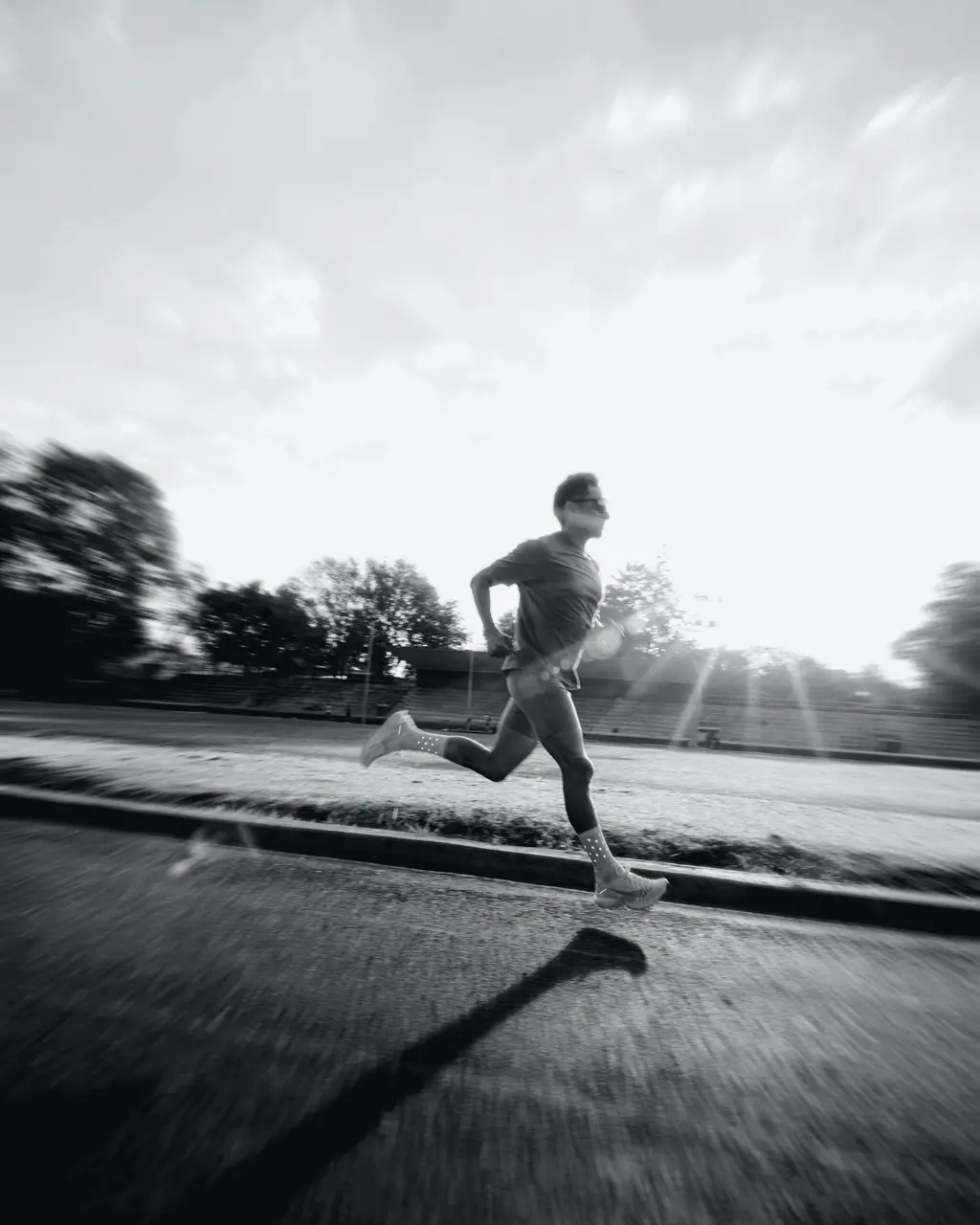 Imagem ilustrativa: pessoa correndo em uma pista de atletismo ao amanhecer, com a luz do sol atravessando o enquadramento.